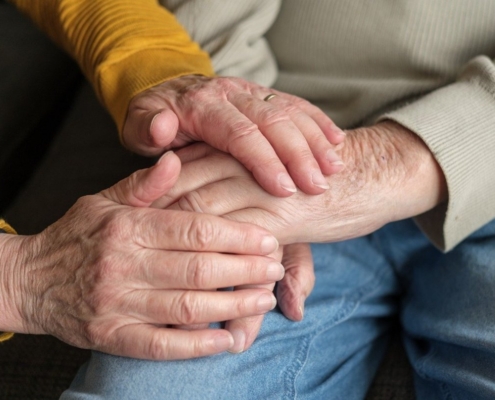 Ältere Frau hält Hand ihres pflegebedürftigen Manns. Nur die Hände sind zusehen.
