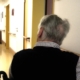 Ältere Mann im Flur eines Pflegeheims und sitzt im Rollstuhl.