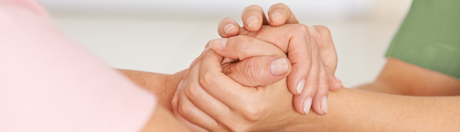 Pflegerin hält Hand einer Seniorin.
