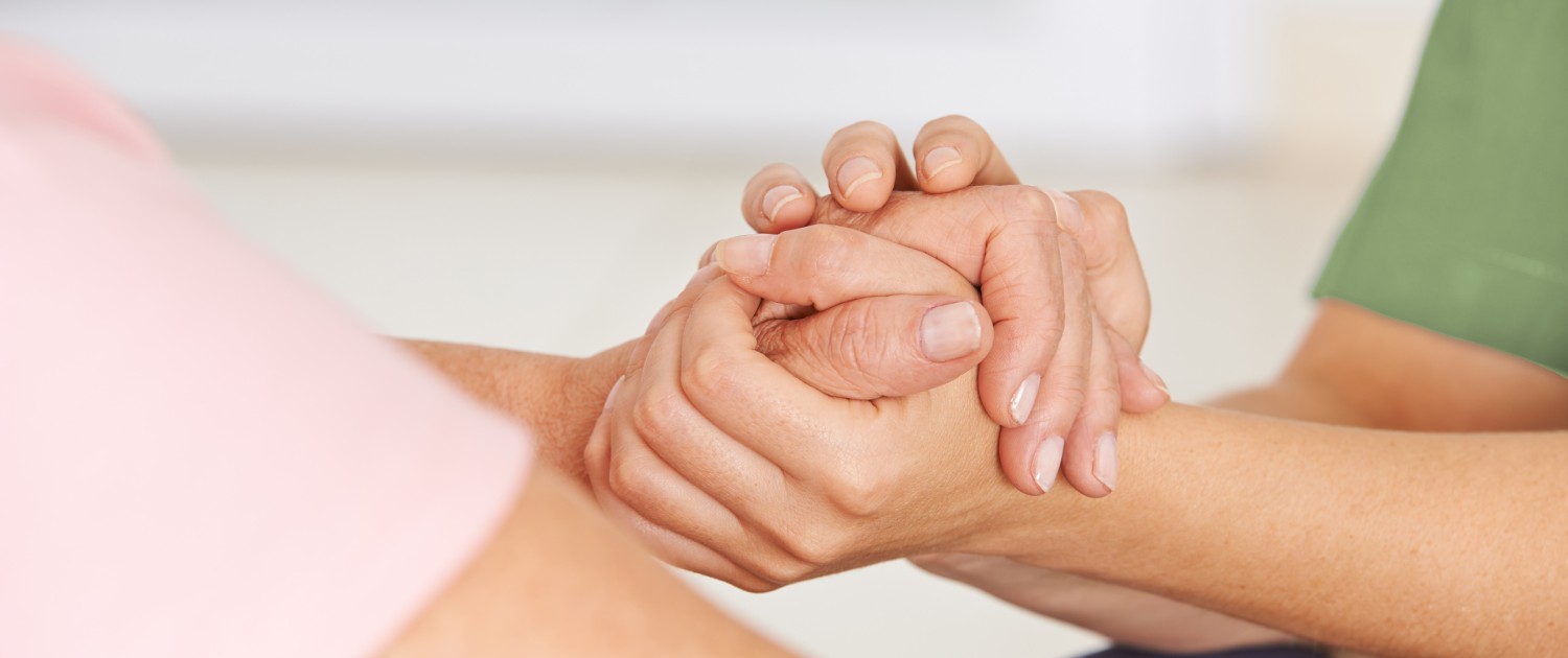 Pflegerin hält Hand einer Seniorin.
